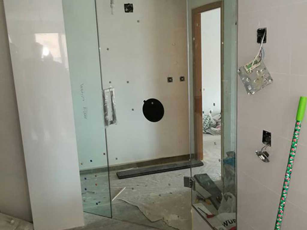 Mampara de baño de cristal templado con puerta abatible en proyecto de reforma. Instalación limpia y funcional.