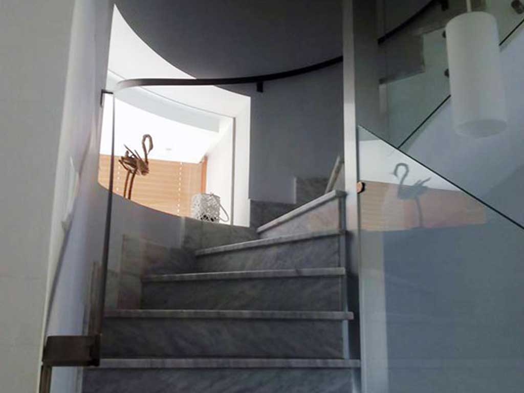 Barandilla de cristal curvada con soportes de acero inoxidable en escalera interior. Seguridad y diseño para viviendas con estilo.