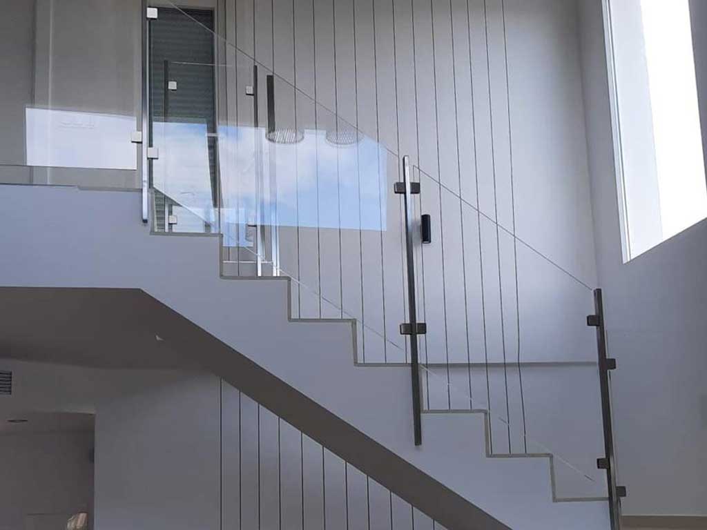 Barandilla de cristal templado con pasamanos de acero inoxidable en escalera recta. Proyecto residencial con acabados minimalistas.