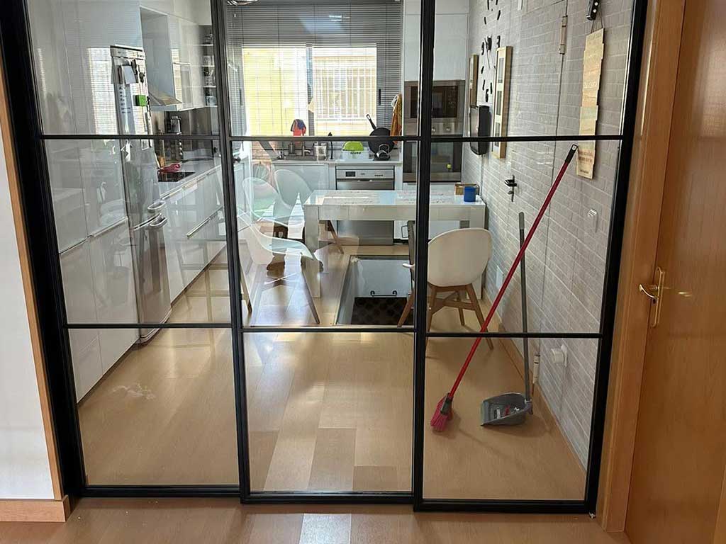 División de espacios en aluminio negro con cristales transparentes. Puerta corredera interior estilo industrial para cocina.